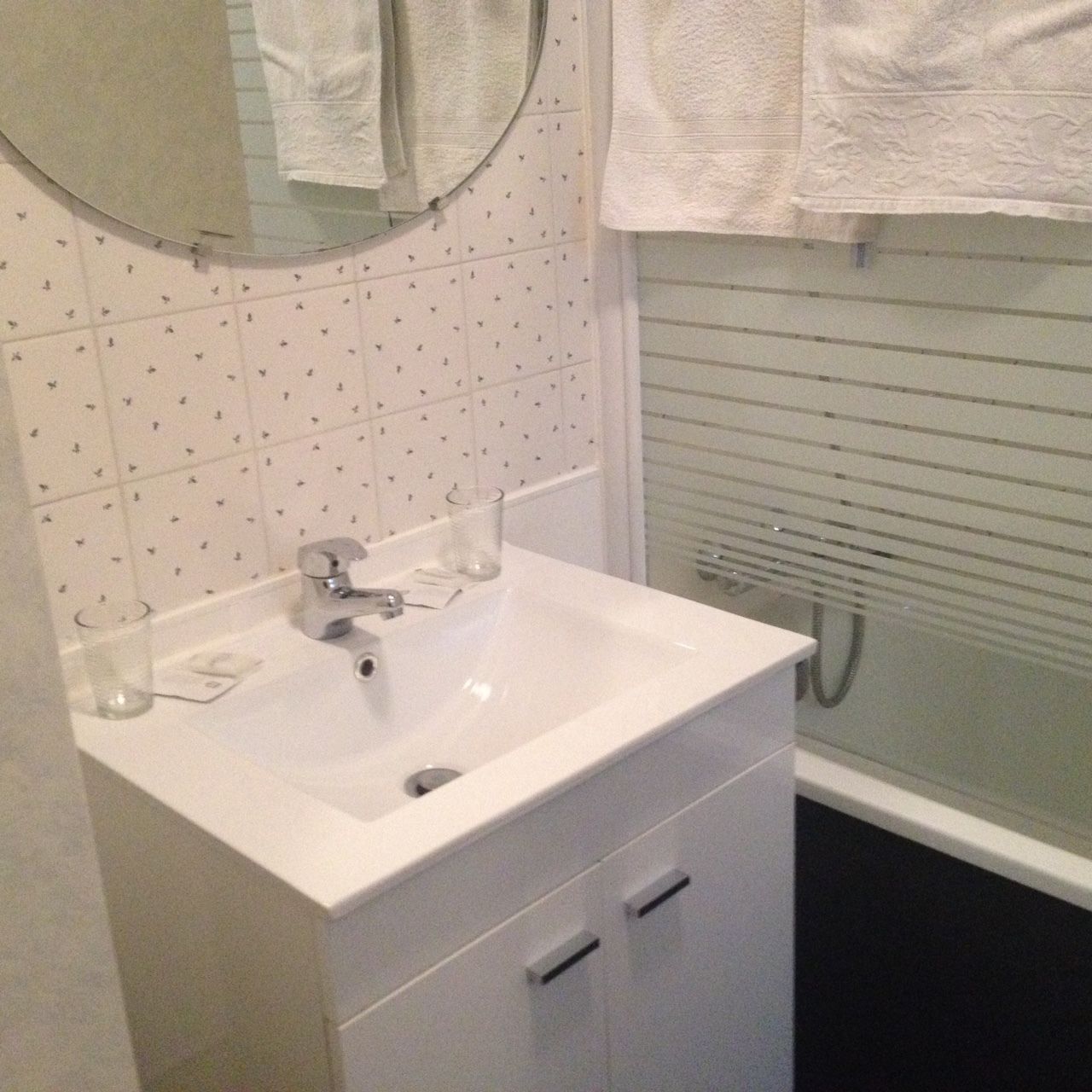 A bathroom with a white sink, two glass cups, a mirror, and a towel rack.
