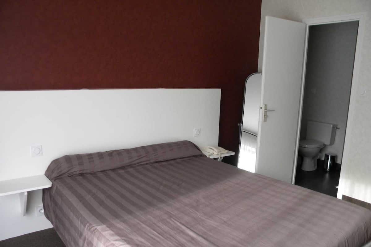 Een eenpersoonskamer met een gestreept beddegoed, een bedtafeltelefoon en een deur naar een badkamer met toilet en wastafel.