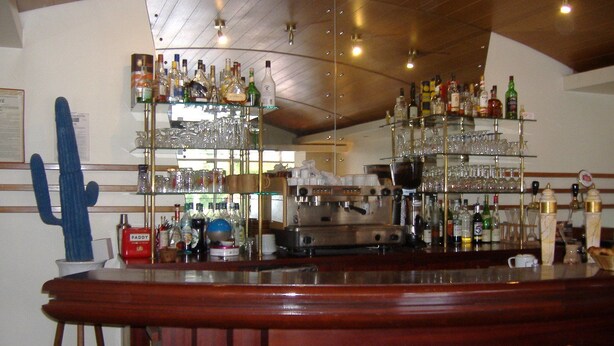 A bar area with multiple shelves of bottles and glasses, a coffee machine, and a wooden bar counter. - Auberge de Pen Mur (Muzillac)