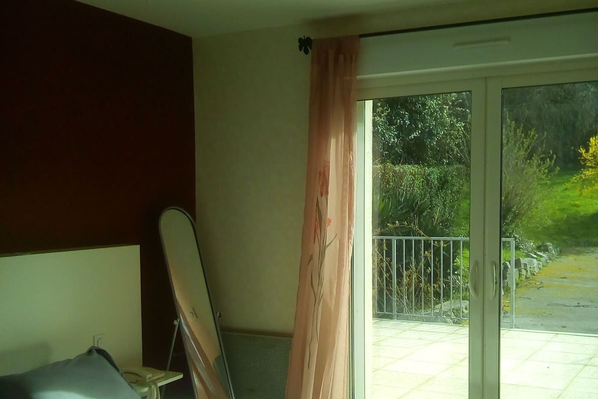 Een slaapkamer met een bed, nachtkastje, telefoon en raam met gordijnen.