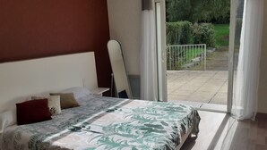 A bedroom with a bed, a nightstand, and a view of a garden through a sliding glass door. - Auberge de Pen Mur (Muzillac)