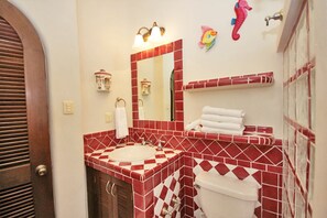 A bathroom with a red and white checkered tile pattern, a white sink, a toilet, and a mirror with wall-mounted lights.