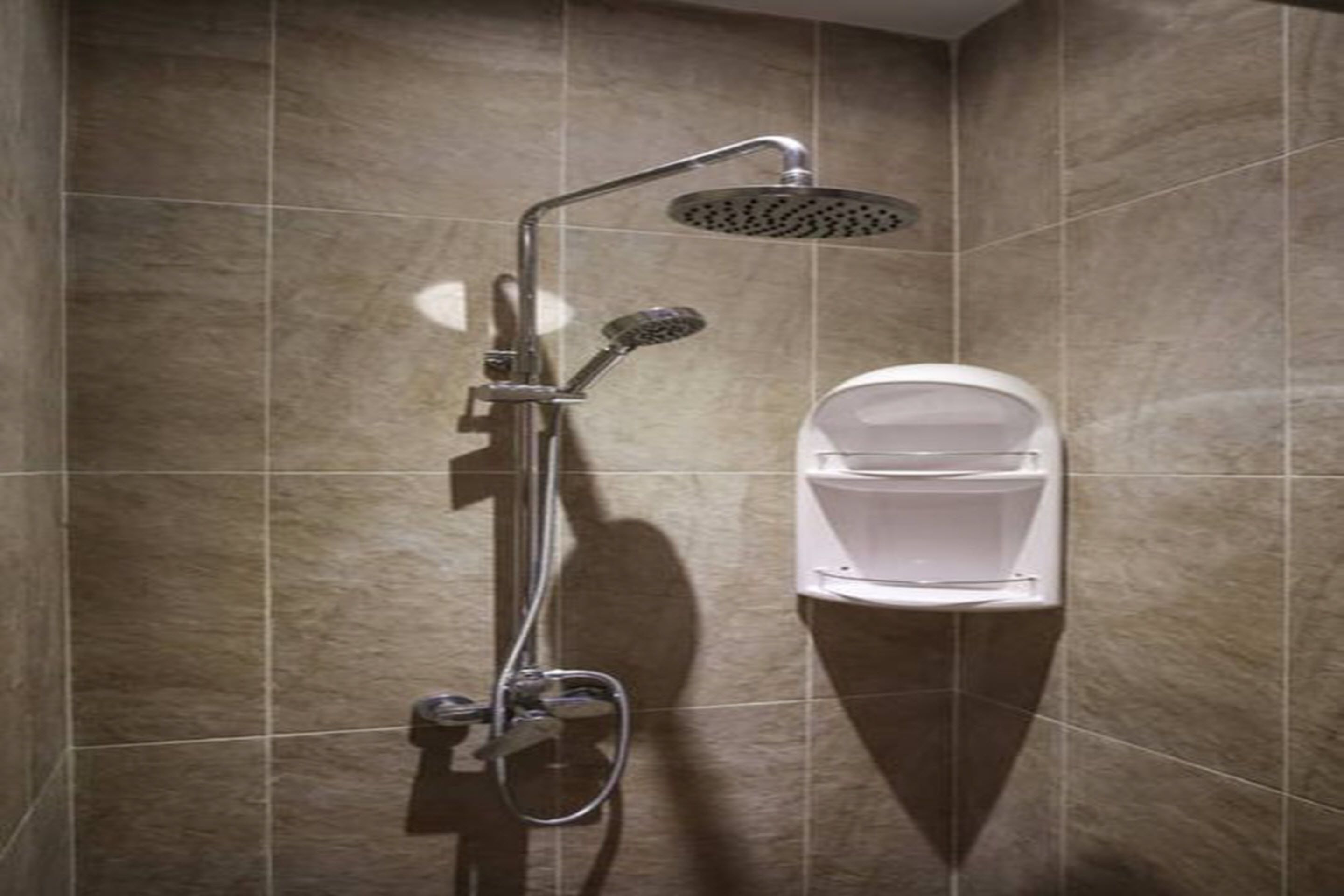 A shower with a handheld showerhead and a wall-mounted toilet in a tiled bathroom.