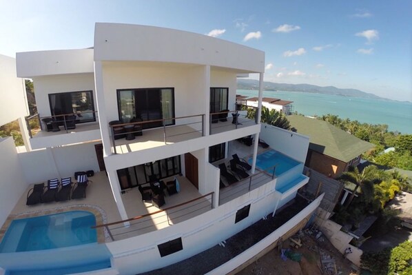Un edificio moderno de varios pisos con piscina, asientos exteriores y vista al mar.