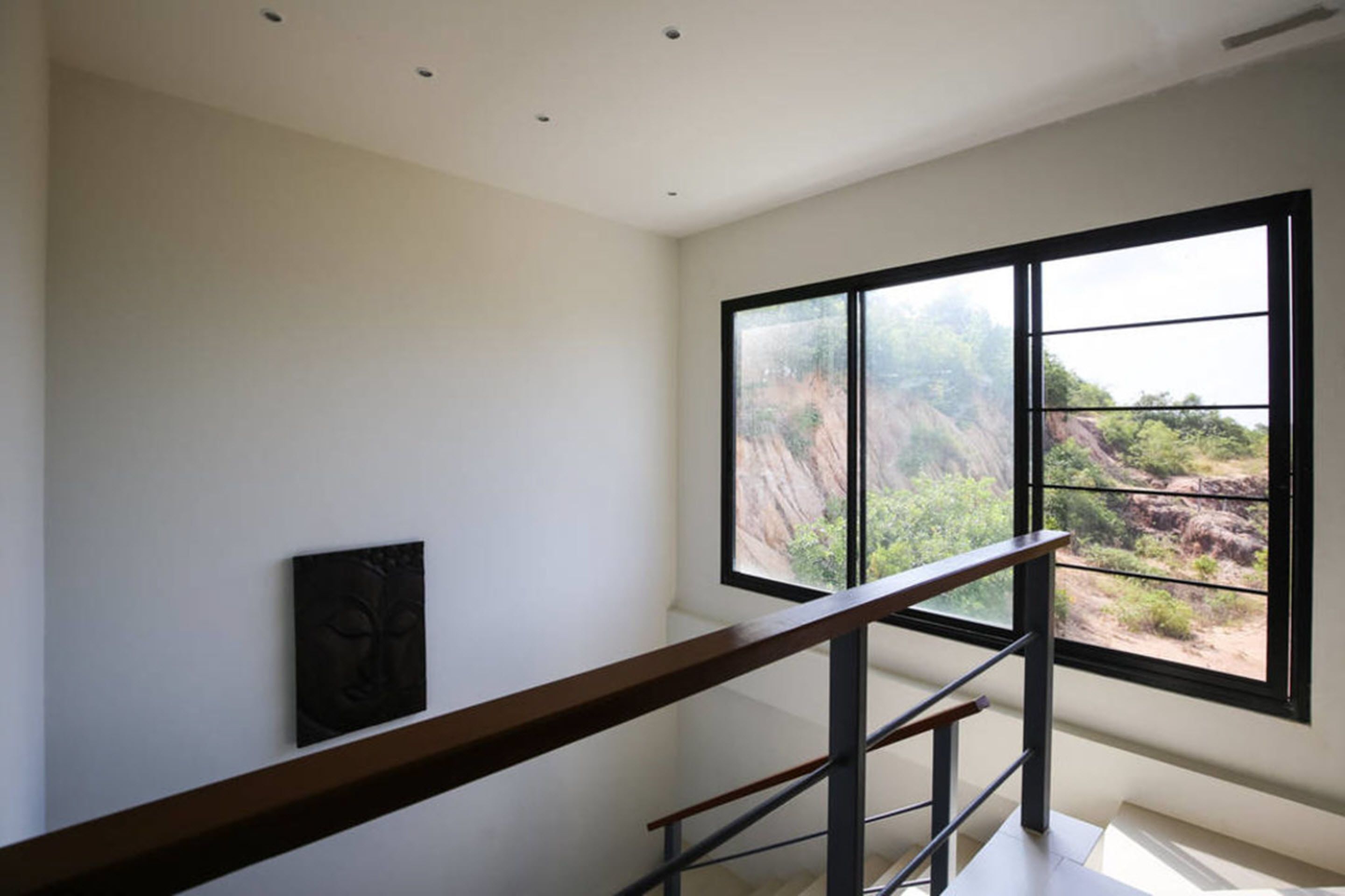 A modern interior with a staircase, a large window with a view of a rocky landscape, and a minimalist wall decoration.