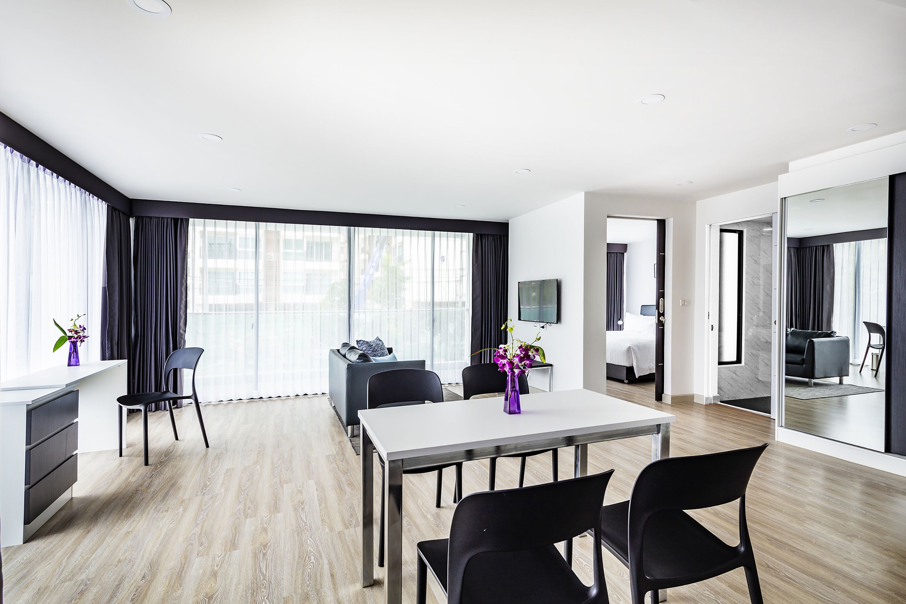 Ett modernt hotellrum med en matplats, en säng, en TV och ett stort fönster med gardiner.