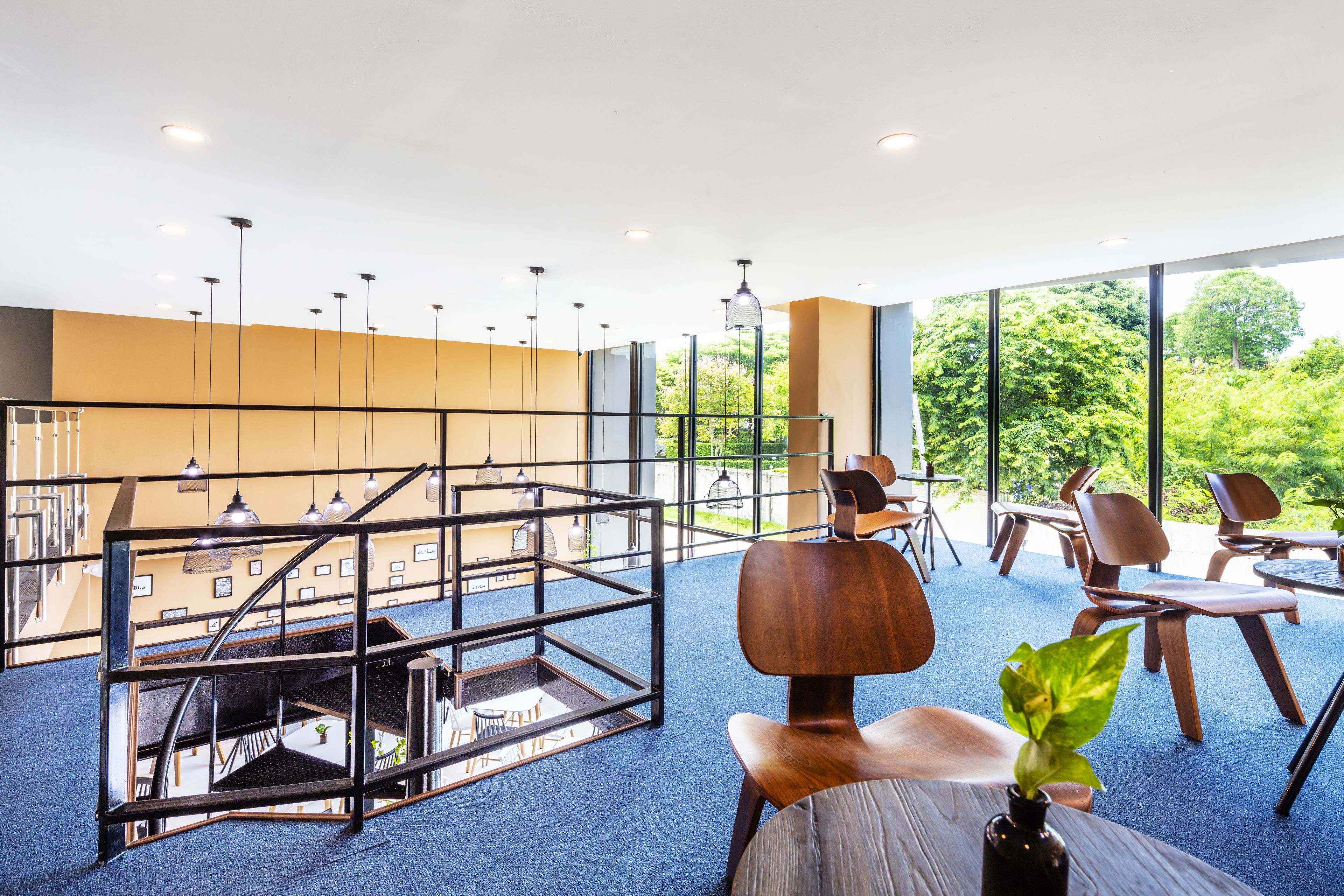 A modern interior with a staircase, seating area, and large windows offering a view of greenery.