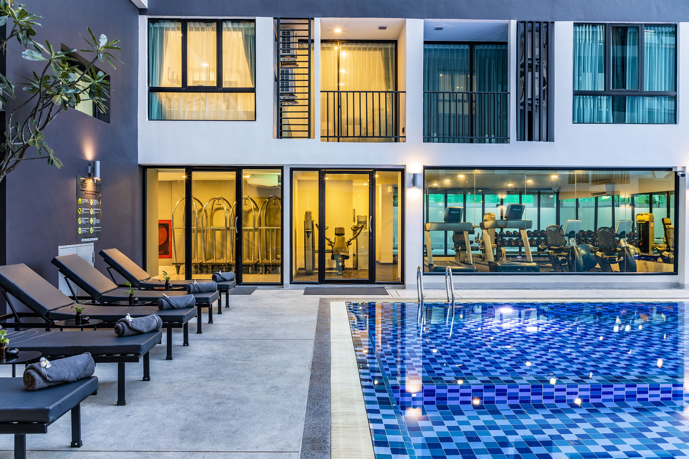 A modern hotel with a swimming pool, sun loungers, and a visible gym area.