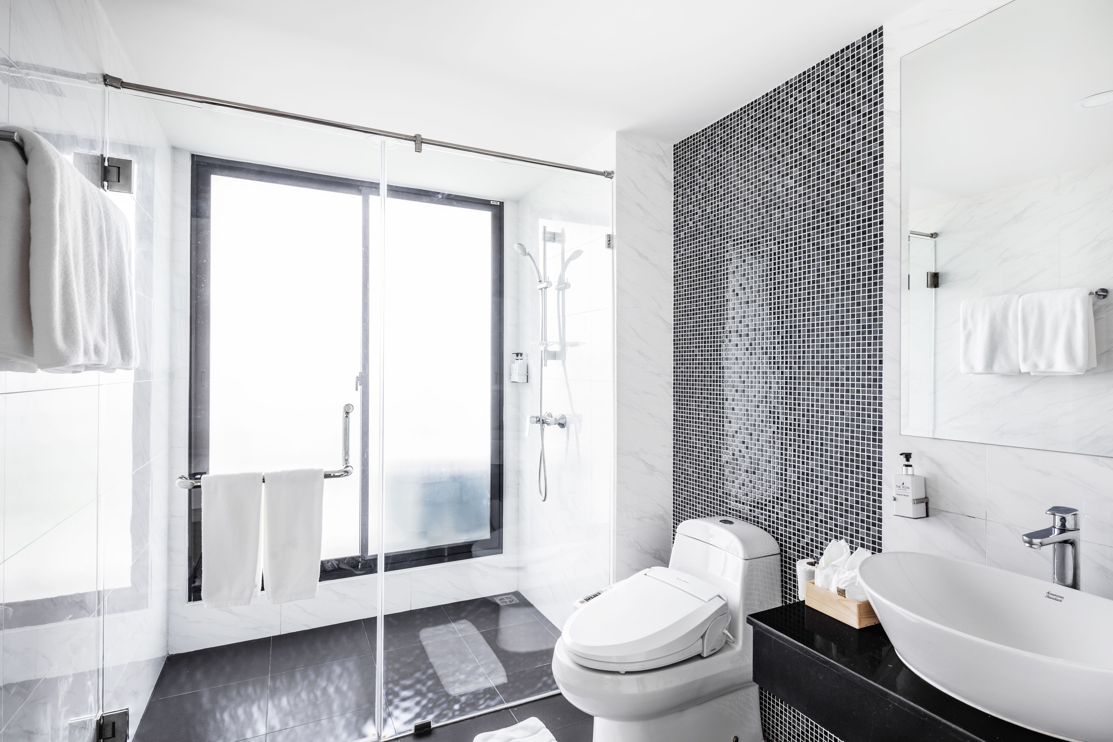 A modern bathroom with a glass shower door, a white toilet, a black sink, and a tiled wall.