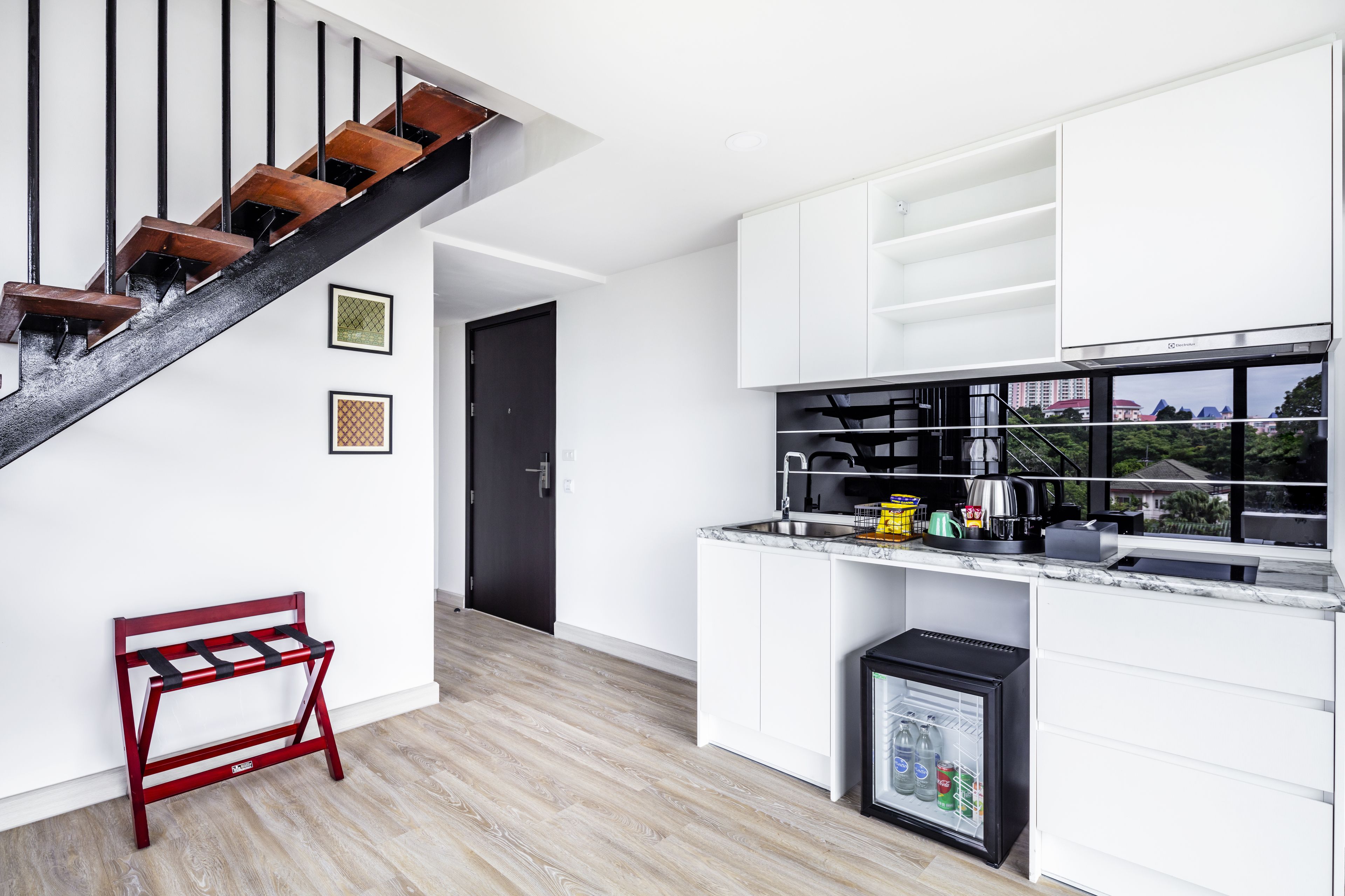Eine moderne Küche mit weißen Schränken, einem schwarzen Kühlschrank und einer Holztreppe.