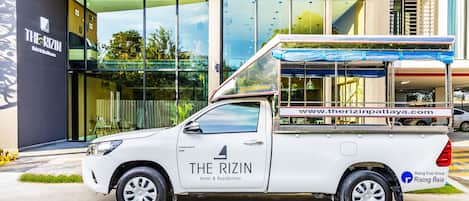 Un camion blanc arborant le logo « The Rizin Hotel & Residences » est garé devant un bâtiment moderne.