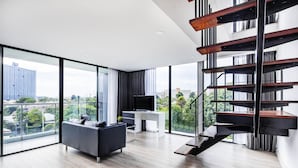 Una sala de estar moderna con un ventanal grande, un sofá gris, un televisor de pantalla plana y una escalera de madera.