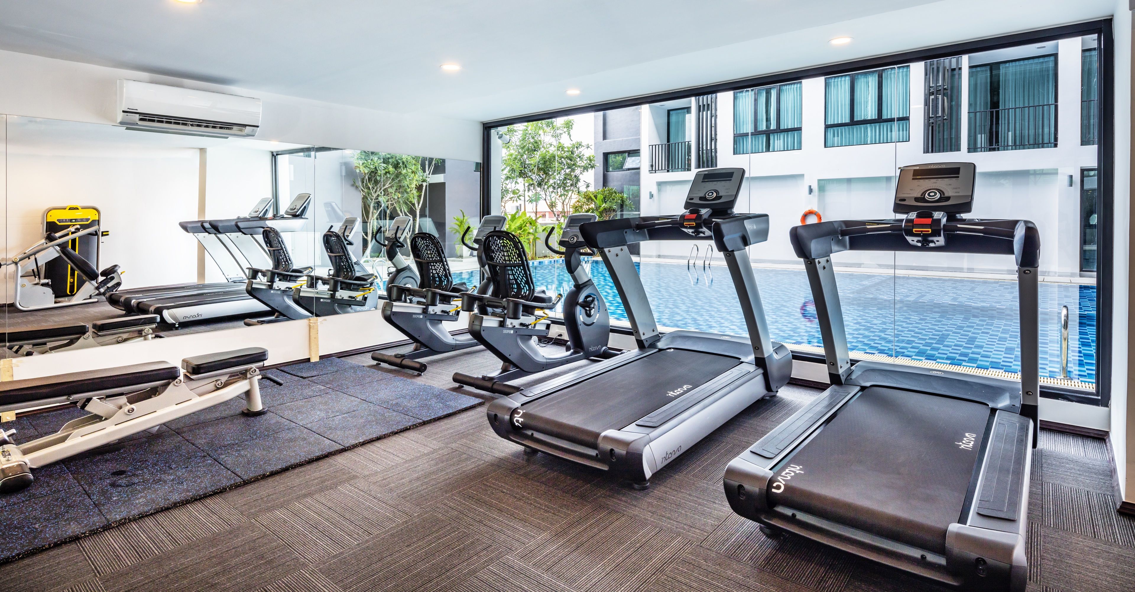 A gym with treadmills, a rowing machine, and a pool in the background.