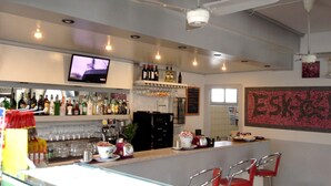 A bar area with a television, shelves of bottles, glasses, and a coffee machine. - Hotel Quadrifoglio (Comacchio)