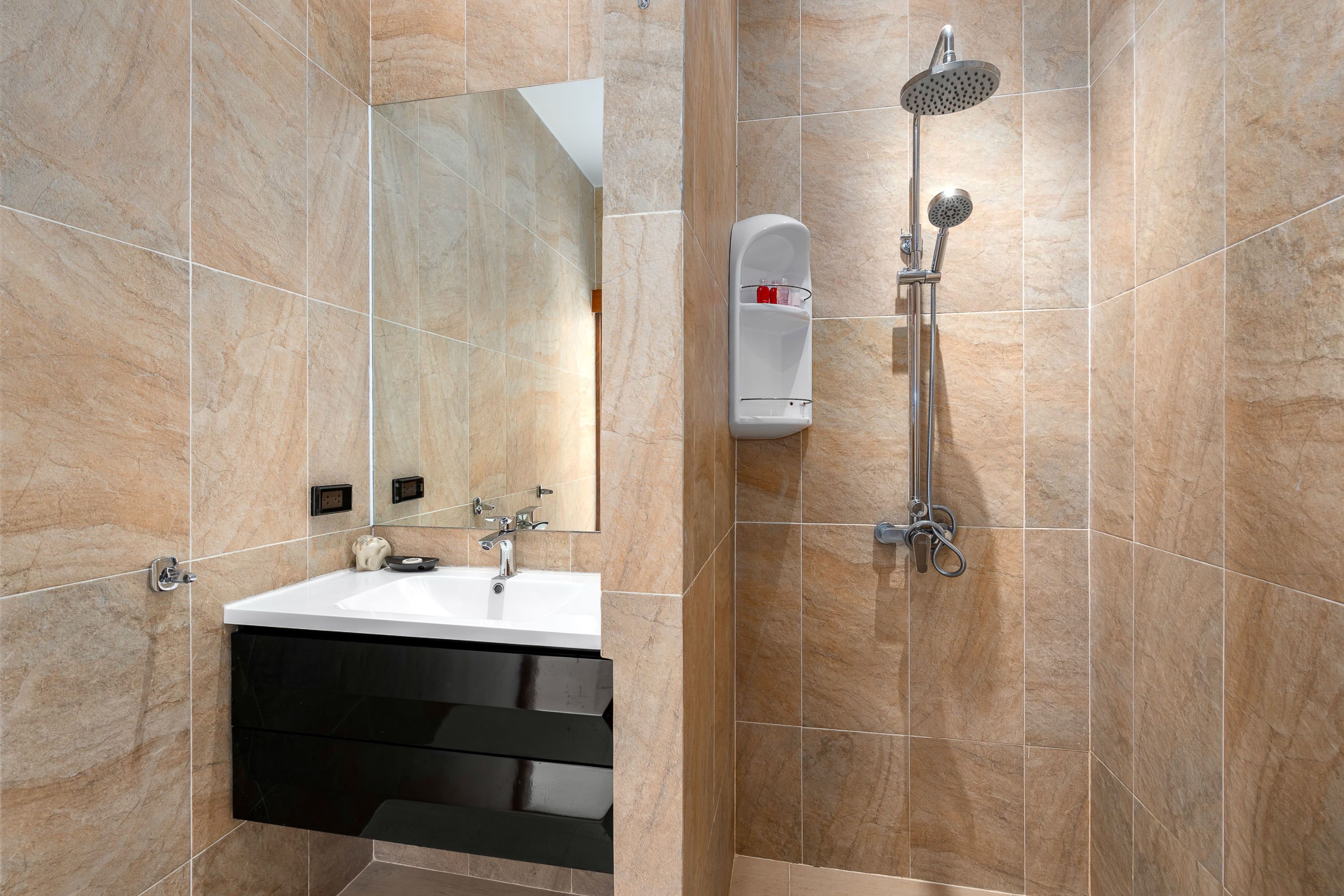 Un baño moderno con lavamanos blanco, mueble negro y cabezal de ducha manual.
