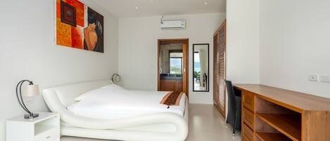 A modern bedroom with a large bed, a bedside table, a desk, and a ceiling fan.