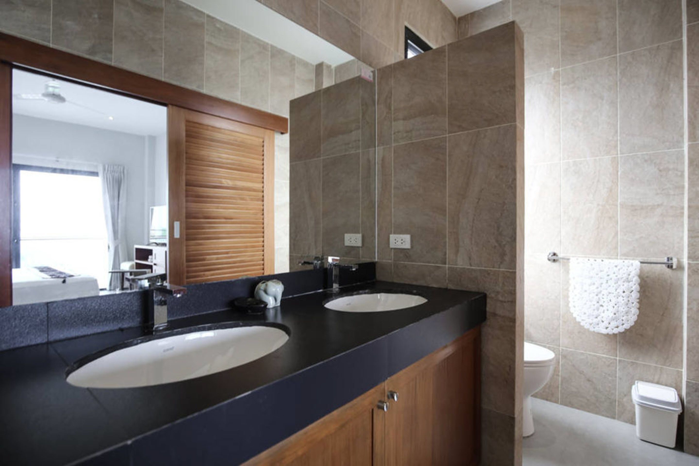 A modern bathroom with two sinks, a large mirror, and a toilet.