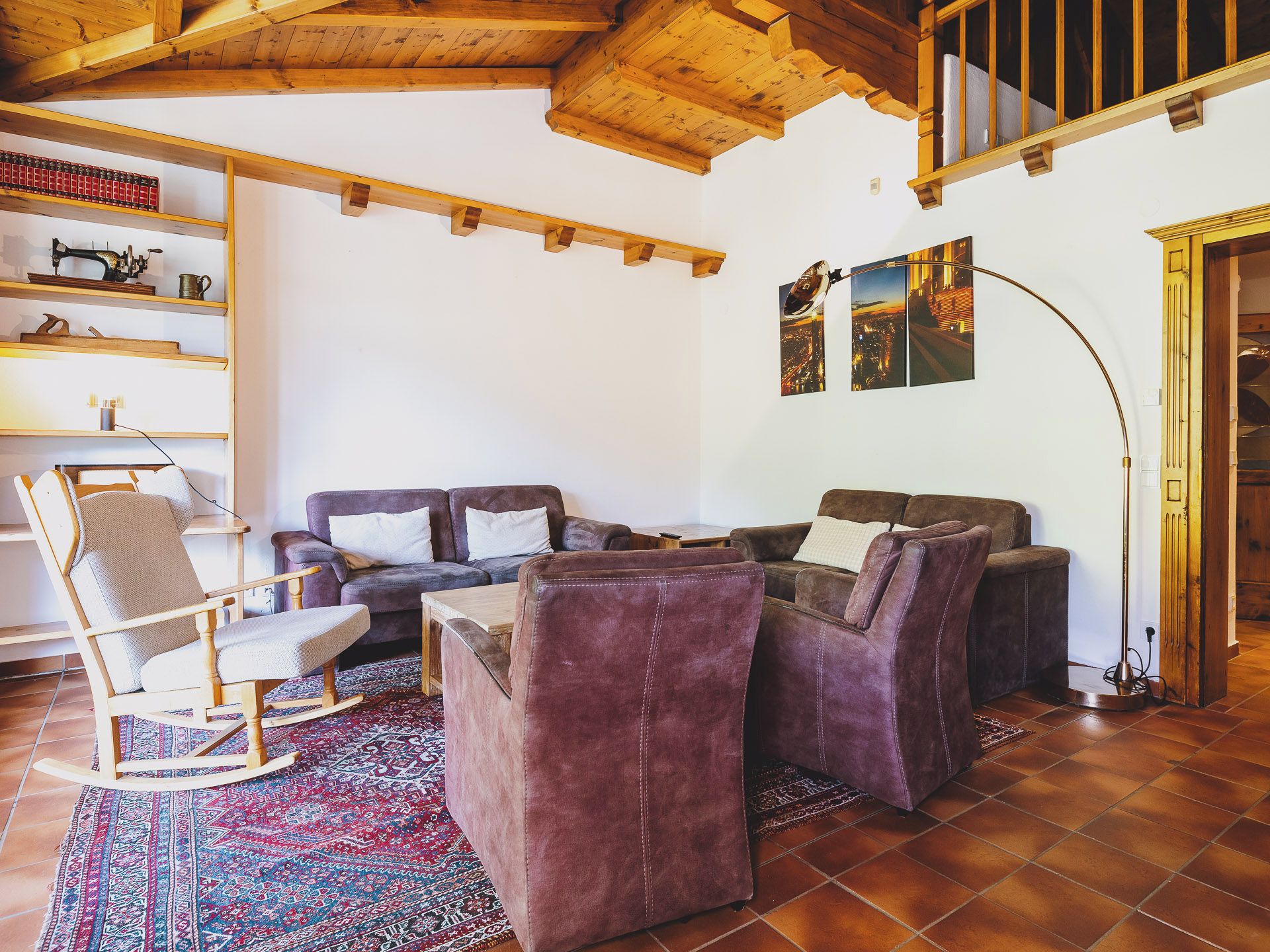 Una sala de estar acogedora con techo de madera, un sillón mecedor, un juego de sofás y una alfombra estampada.
