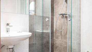 Un baño moderno con ducha acristalada, lavabo blanco y espejo.