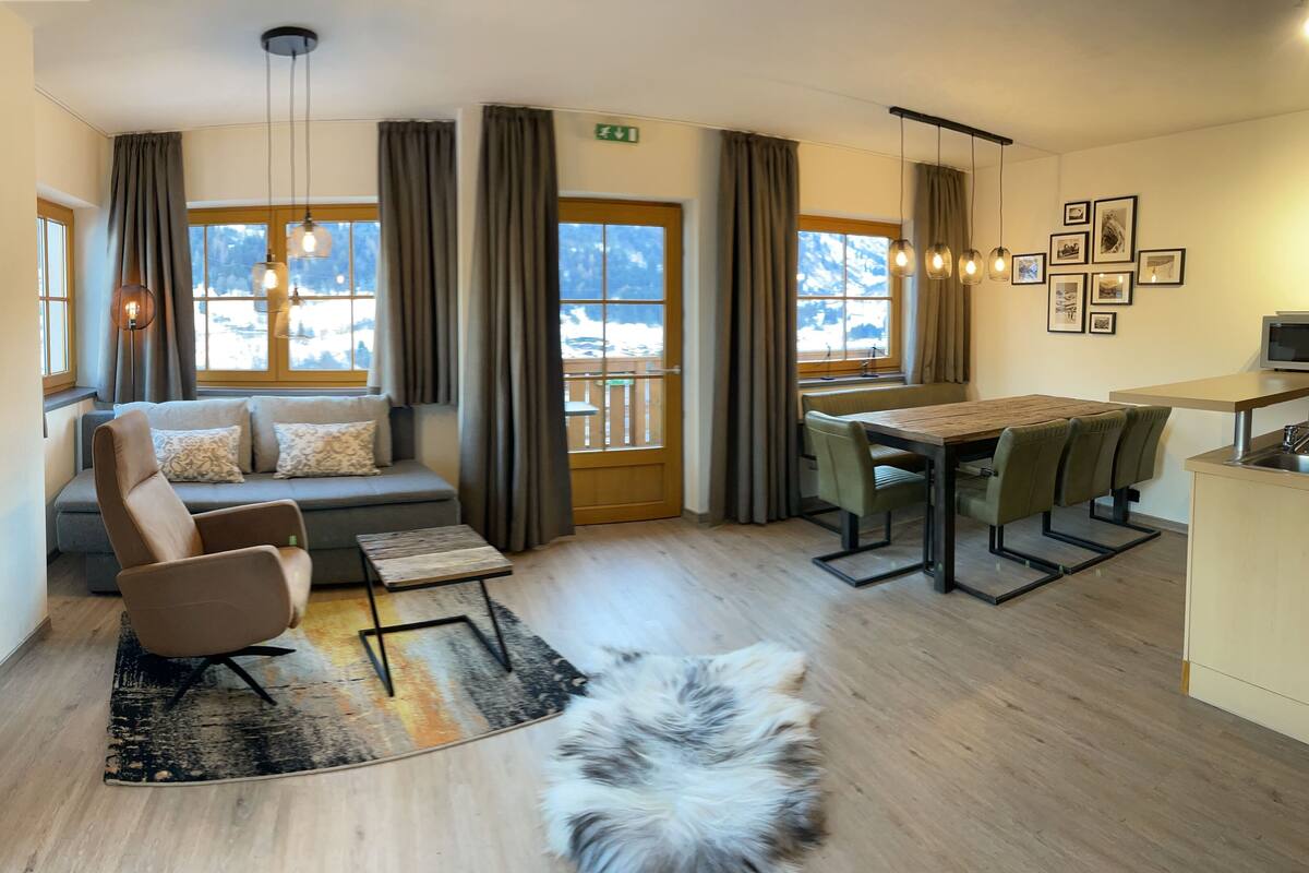 Un salon confortable avec un canapé, une petite table et un chien. On y trouve également une table à manger avec des chaises et un coin cuisine équipé d’un four à micro-ondes.
