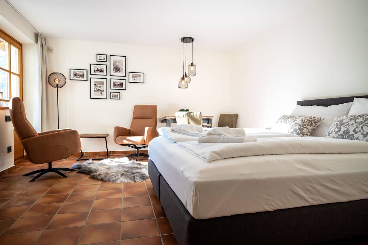 Une chambre d’hôtel avec un grand lit, deux fauteuils, un bureau et une lampe sur pied.