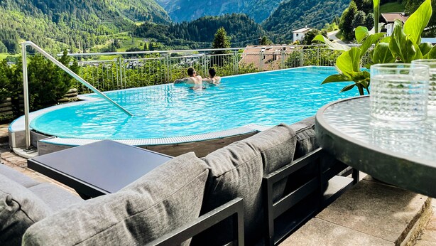 A pool with a mountain view, outdoor seating, and a glass table.