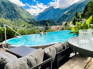 Piscina con vista a la montaña, mobiliario exterior y una mesa de vidrio.