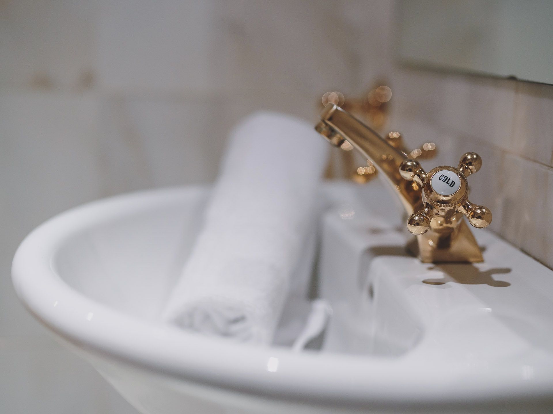 A bathroom sink with a gold faucet and a rolled towel.