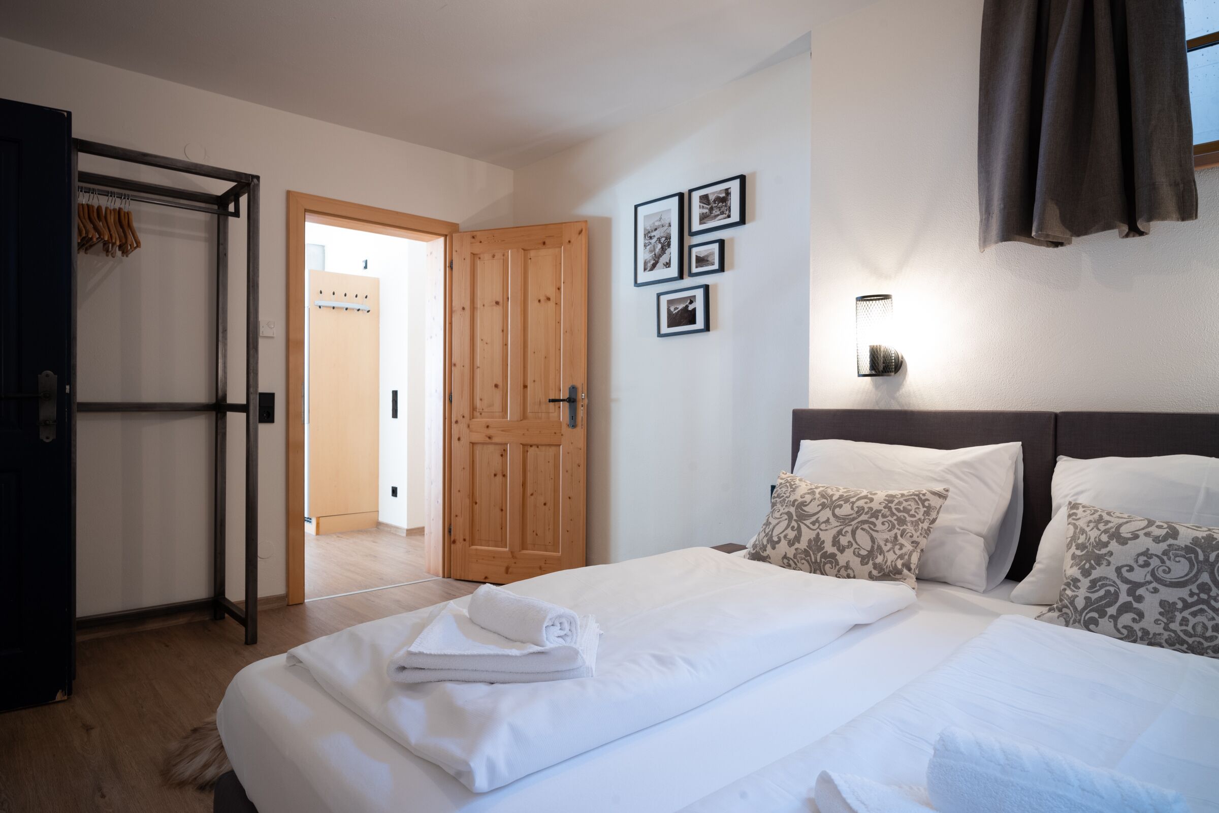 Habitación de hotel con puerta de madera, cama con ropa de cama blanca, almohadas estampadas y lámpara de pared.