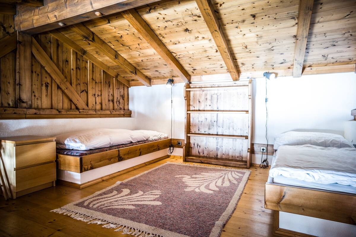 Une chambre dans une cabane en bois, avec un lit en mezzanine, une table de chevet et une grande fenêtre.
