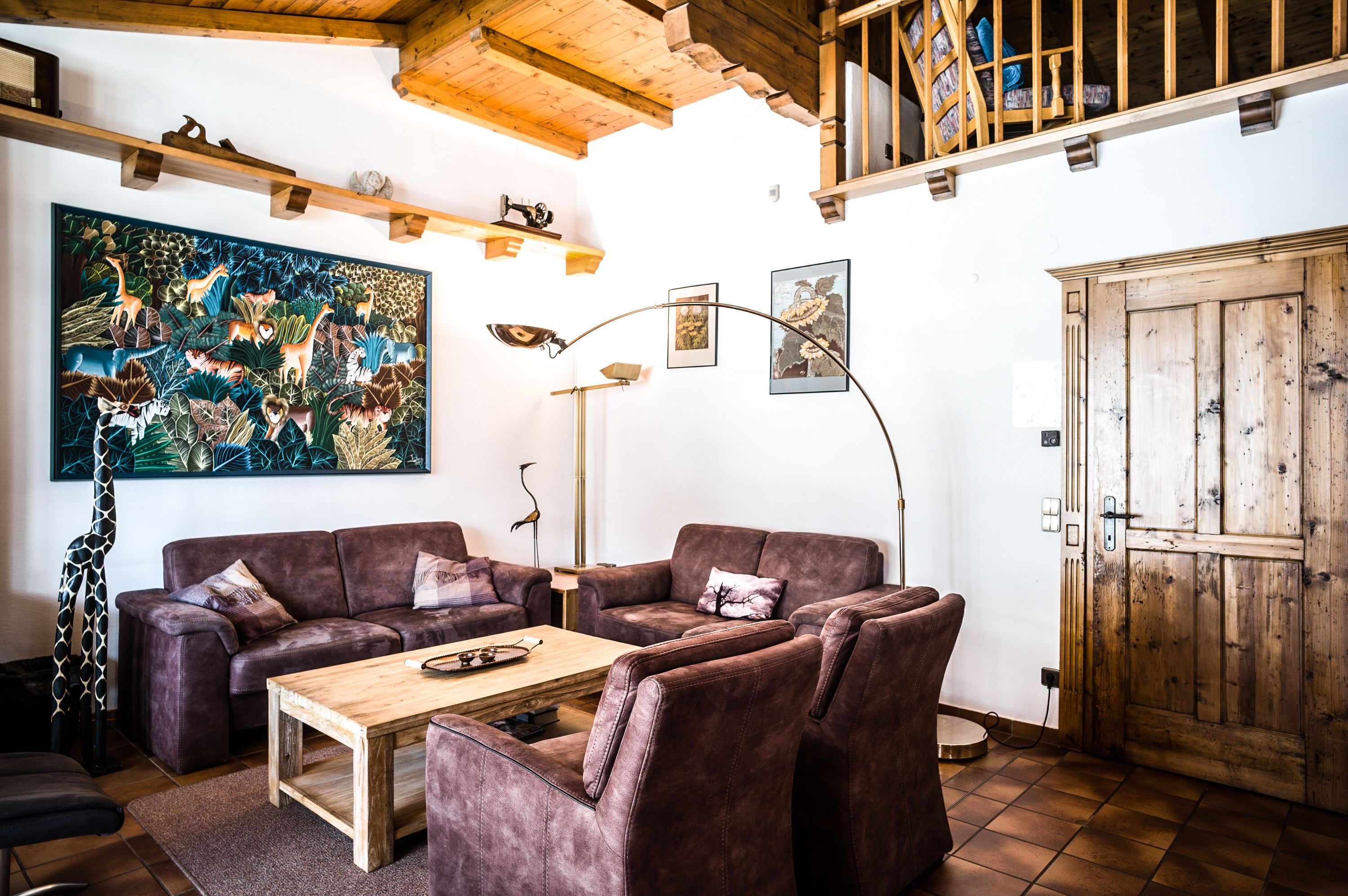 Un salon chaleureux avec un canapé d’angle, une table basse en bois et un grand tableau représentant des animaux accroché au mur.