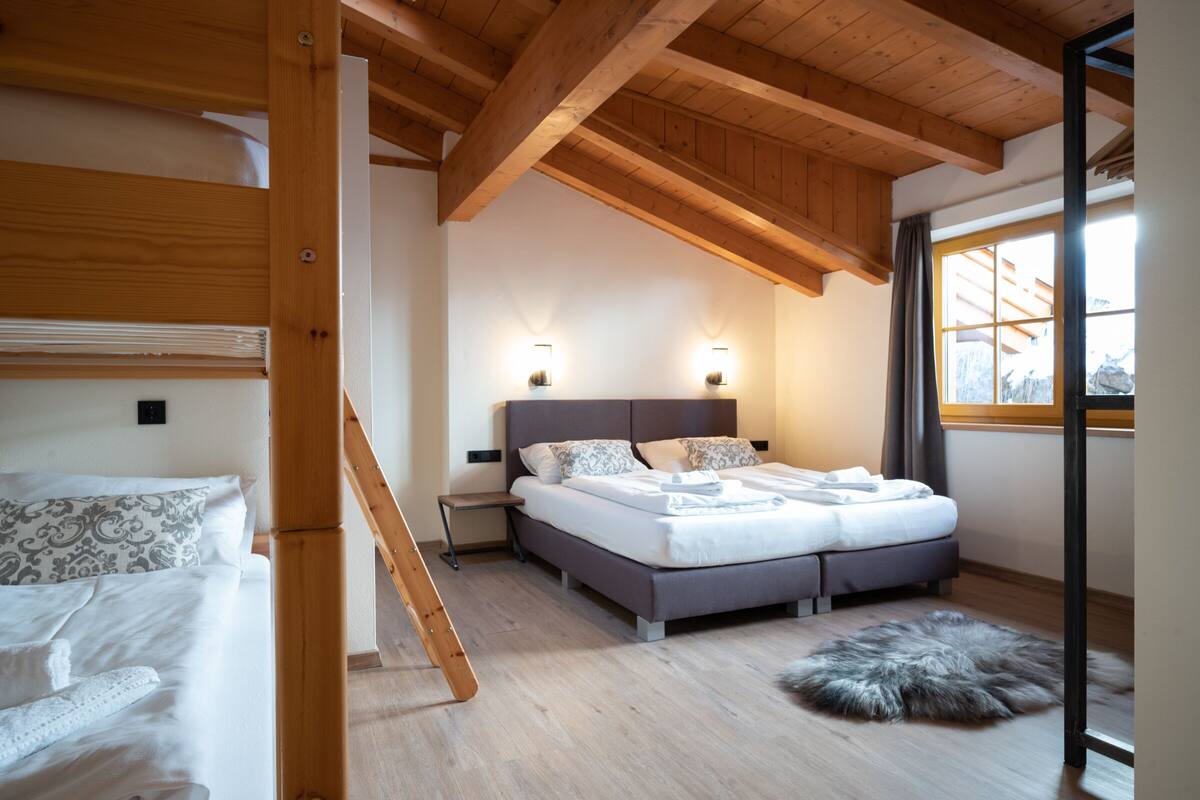 Une chambre avec un plafond en bois, un lit agrémenté d’oreillers à motifs, un tapis moelleux et une table de chevet.