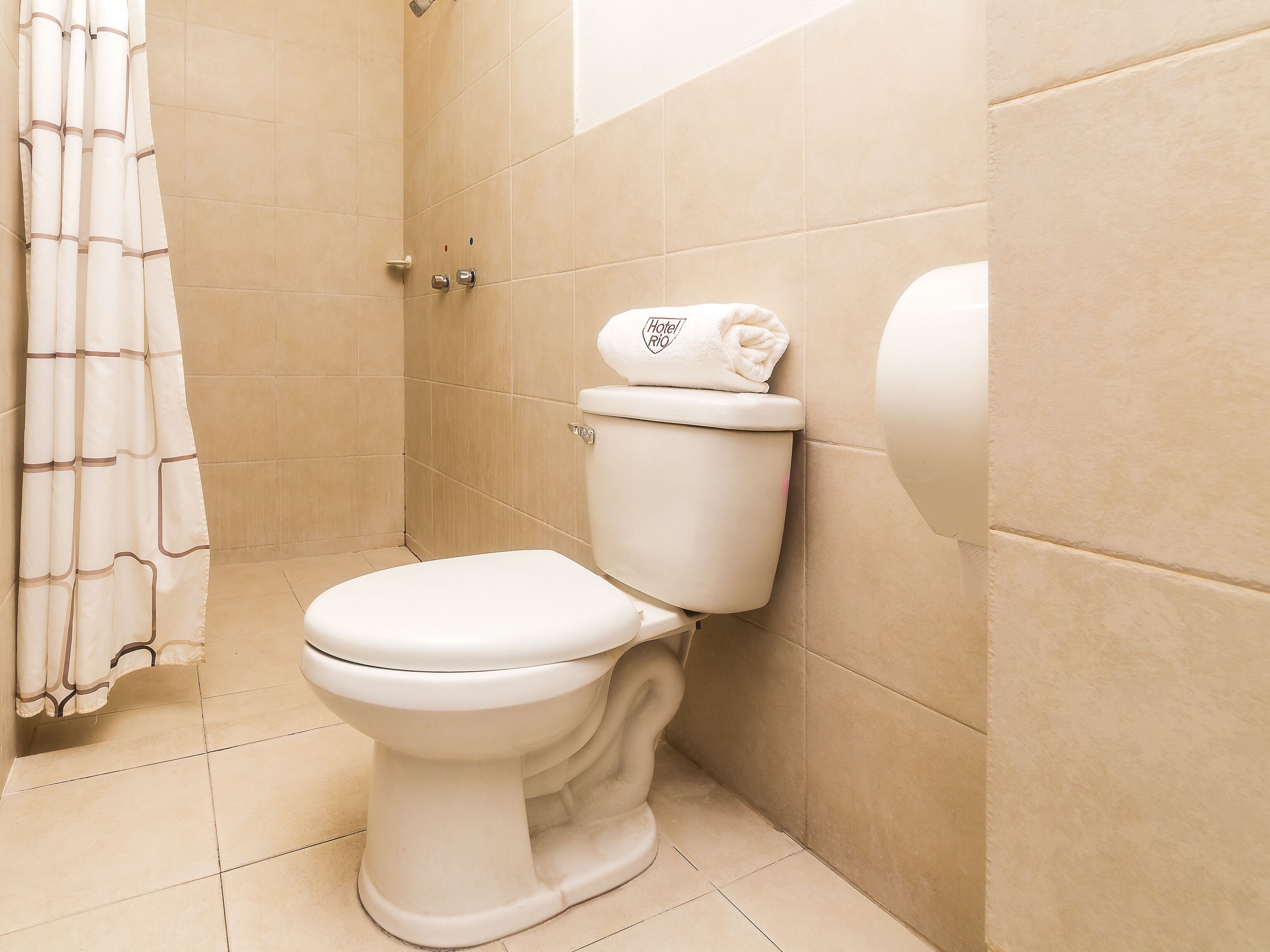 Un baño con inodoro, cortina de ducha y una toalla sobre el inodoro.