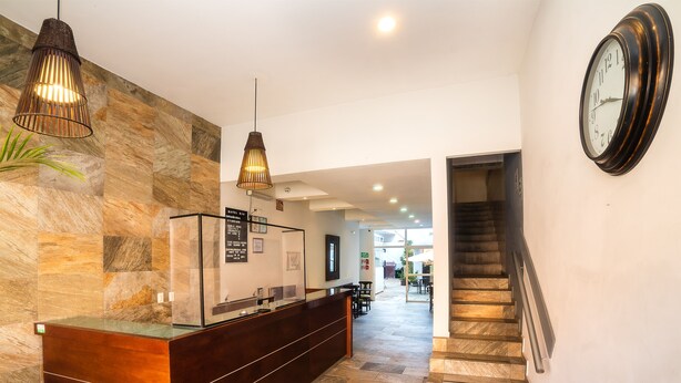 A reception area with a stone wall, a wooden reception desk, a hanging light fixture, and a clock on the wall. - Hotel Río Puebla Centro (Puebla)