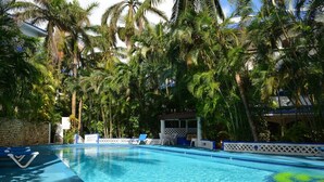 A swimming pool with clear blue water, surrounded by palm trees and a covered seating area. - Natz Ti Ha H101 by PRP (Playa del Carmen)