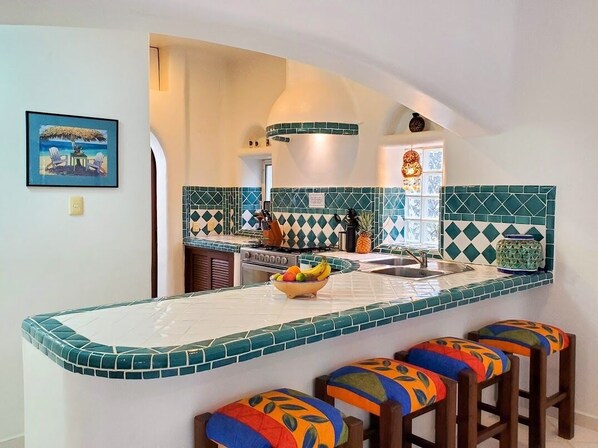 Una cocina con una isla central, taburetes de colores y un salpicadero decorativo.