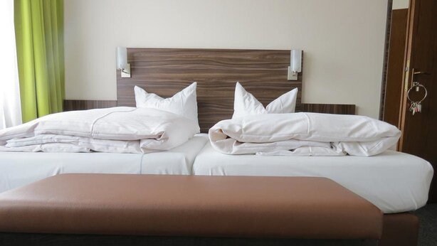 A double bed with white linens and pillows, a wooden headboard, and a bench in front. - Hotel zum Stern (Baumholder)
