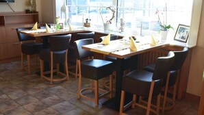 A restaurant with multiple tables and chairs, a tiled floor, and a window with a view of the street. - Hotel zum Stern (Baumholder)
