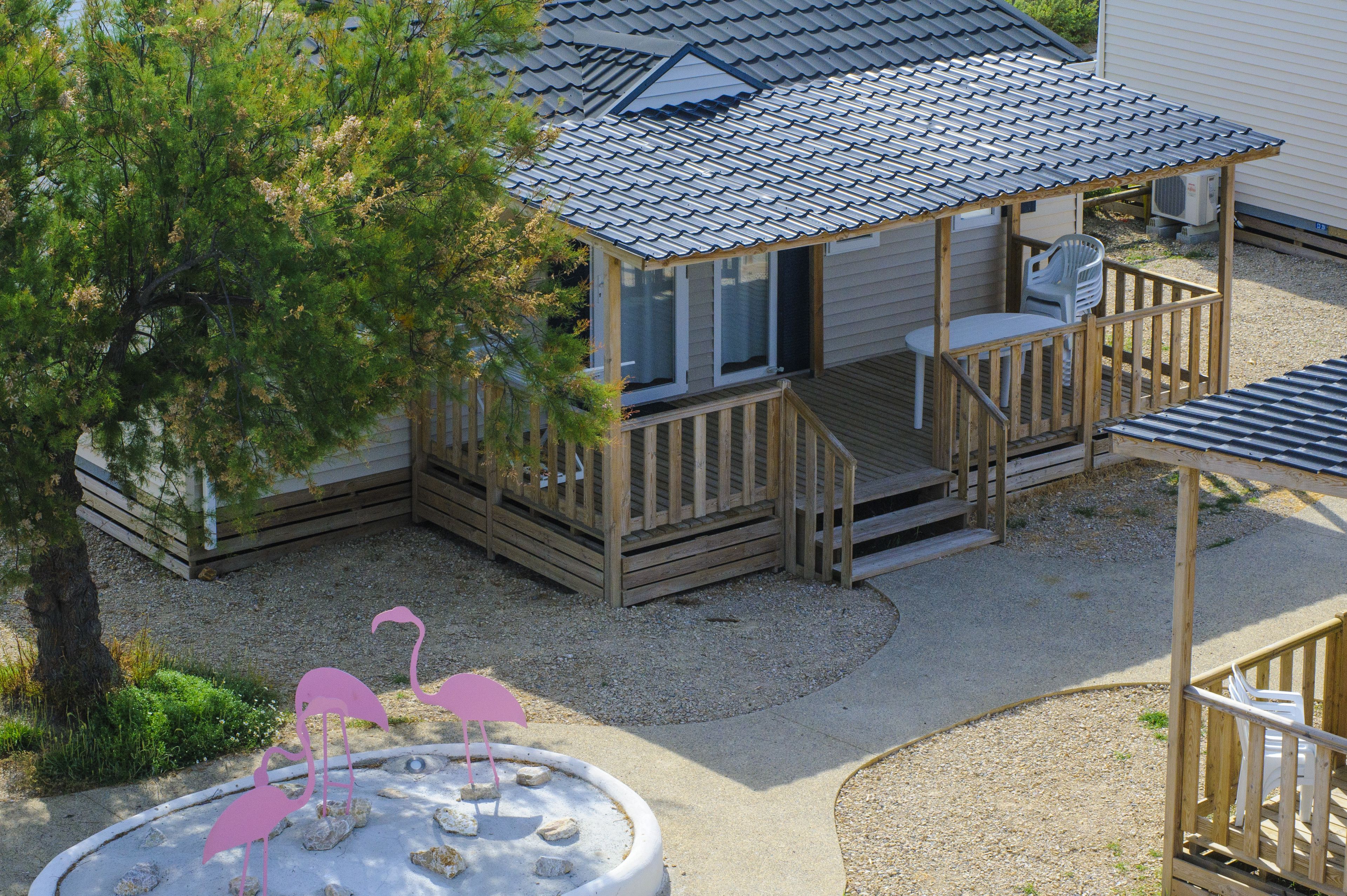 A wooden deck with a covered seating area, a small pool with flamingos, and a tree in the background.