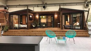 A modern, spacious building with a covered outdoor area featuring two turquoise chairs and a small table. - Camping Le Clos du Rhône (Saintes-Maries-de-la-Mer)