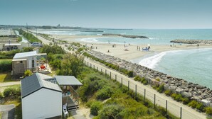 A coastal view with a sandy beach, rocky shoreline, and a fenced pathway. - Camping Le Clos du Rhône (Saintes-Maries-de-la-Mer)