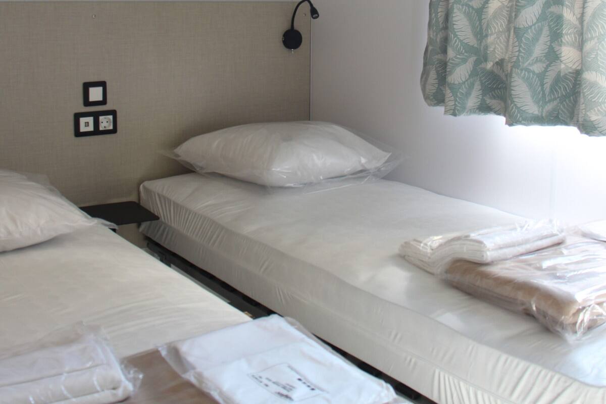 Une chambre d’hôtel avec deux lits simples, une petite armoire et une fenêtre avec un rideau à motifs de feuilles.