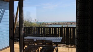 A wooden deck with a table and chairs, overlooking a rocky shoreline and a body of water. - Camping Le Clos du Rhône (Saintes-Maries-de-la-Mer)