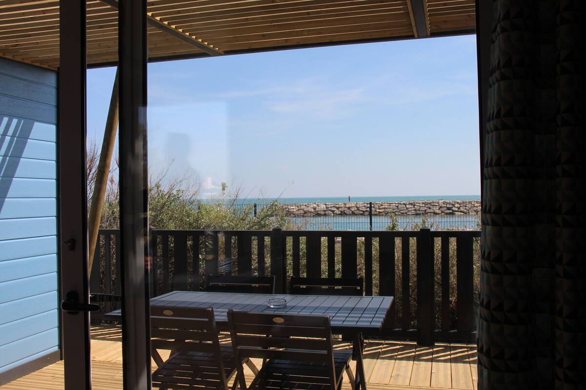Une terrasse en bois avec une table et des chaises, donnant sur une côte rocheuse et une étendue d’eau.