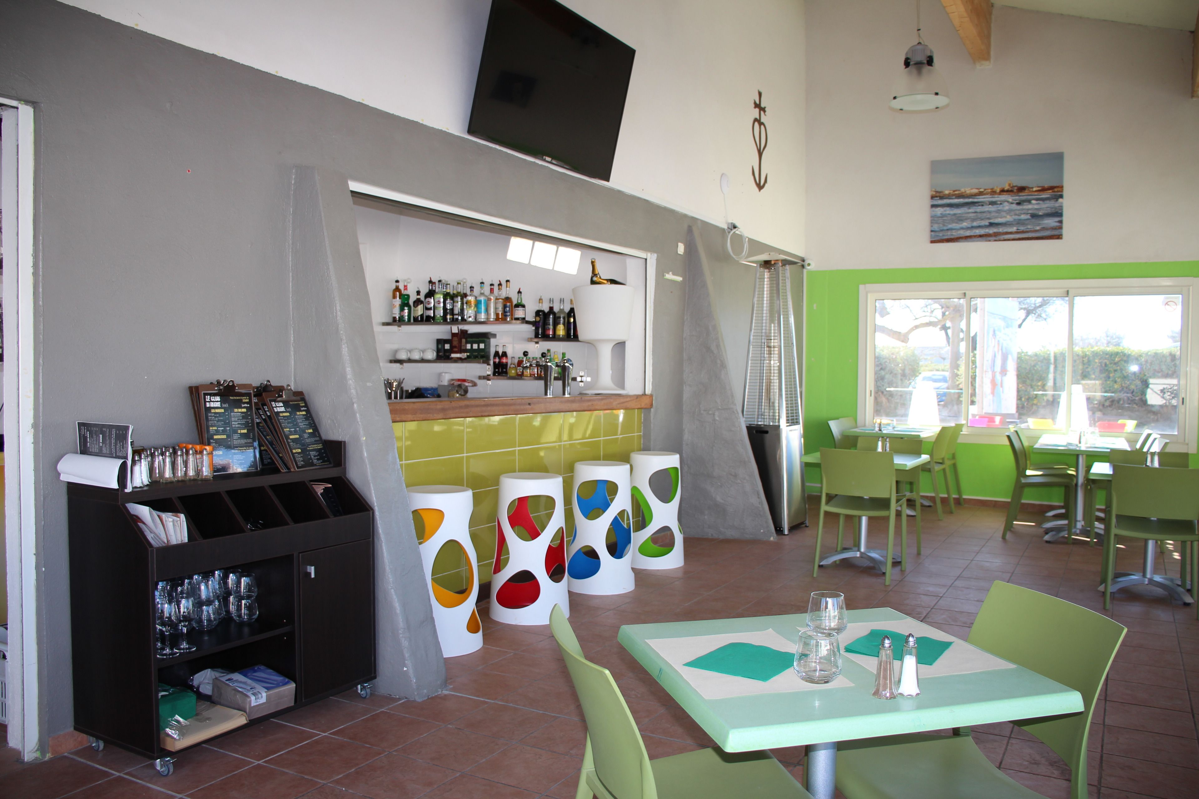 A restaurant with a bar area, green chairs, and a tiled floor.