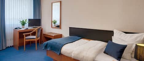 A hotel room with a bed, a desk with a chair, a television, a mirror, and a lamp.