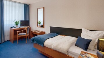 A hotel room with a bed, a desk with a chair, a television, a mirror, and a lamp.