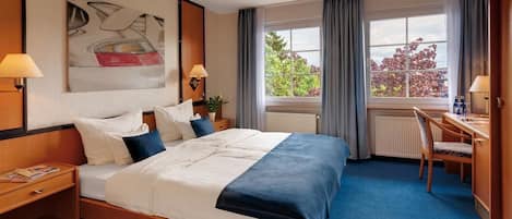 Habitación de hotel con una cama grande, dos mesitas de noche con lámparas, un escritorio con silla y una ventana con cortinas.