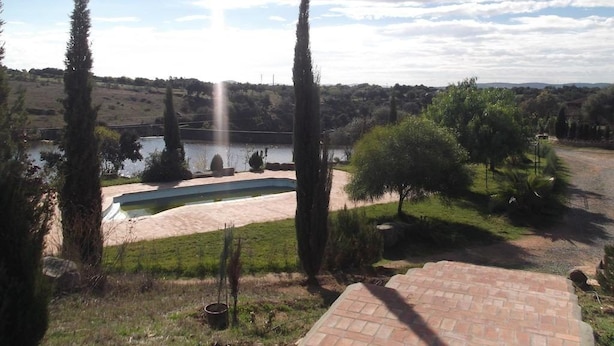Un área exterior ajardinada con piscina, árboles y vista a un lago.
