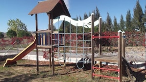 Un parque infantil con tobogán, red de escalada y un pequeño refugio.
